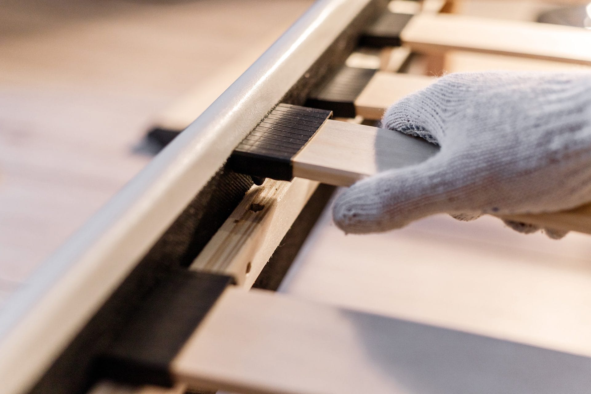 Een hand met werkhandschoen die een lattenbodem van een aangepast bed vasthoudt.